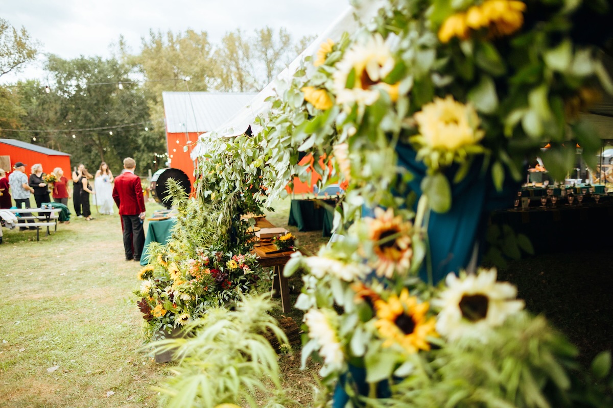 Floral installation leading into a wedding reception tent in Minnesota featuring sunflowers and cannabis plants, designed by an award-winning Minnesota wedding planner.