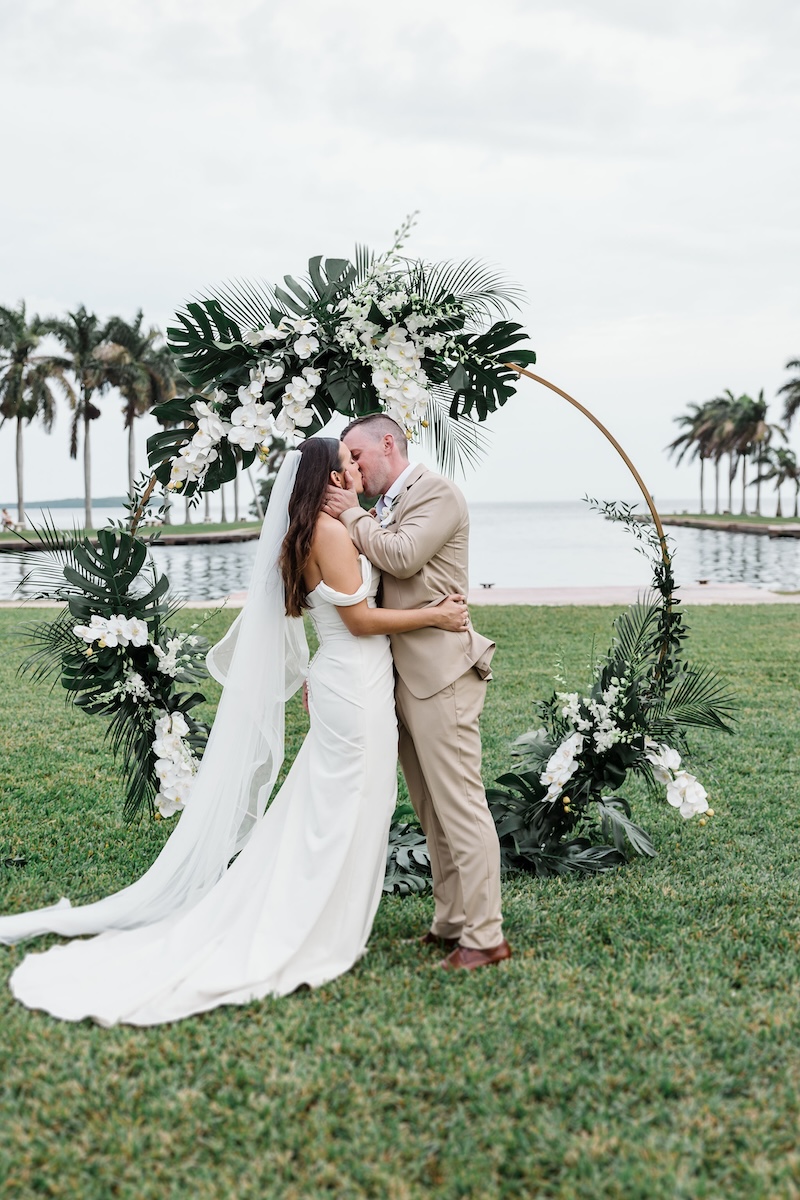 Oceanfront wedding ceremony at Deering Estate in Miami, FL in classic white and green tropical florals with circle arch backdrop on ocean.